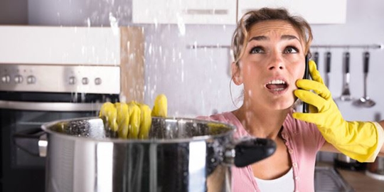 woman on the phone holds a pot under a leak