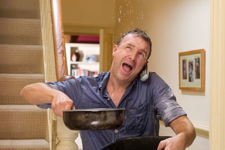 man on the phone holding pots under a leak
